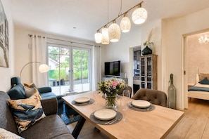 Un salon moderne comprenant un coin repas, un ensemble de canapés, un téléviseur et un meuble agrémenté d’objets décoratifs.