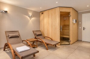 Une salle de sauna équipée de deux chaises longues en bois, d’une petite table en bois et d’un coffre de sauna.
