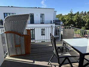Relax on the balcony with a wicker chair and metal chair, surrounded by lush greenery and a view of the adjacent building.