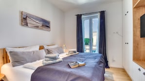 Una cama bien hecha con una manta morada, una mesita de noche con una lámpara y una ventana con cortinas.