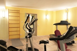 Une salle de sport équipée de matériel d’exercice, avec une échelle en bois et une porte donnant sur une autre pièce.