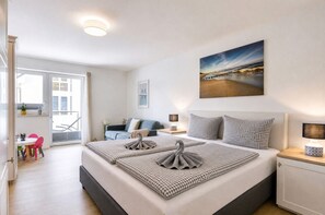 Una camera d'hotel con un letto, un quadro, vista sulla spiaggia, un balcone e un'area ristoro.