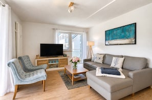 Una sala de estar con sofá, sillón, televisor, mesa de centro de madera y un cuadro en la pared.