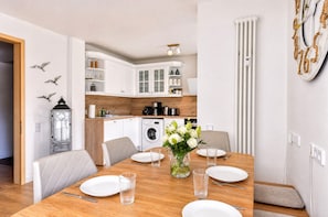 Una cocina moderna con armarios blancos, lavadora y un comedor con mesa para dos.