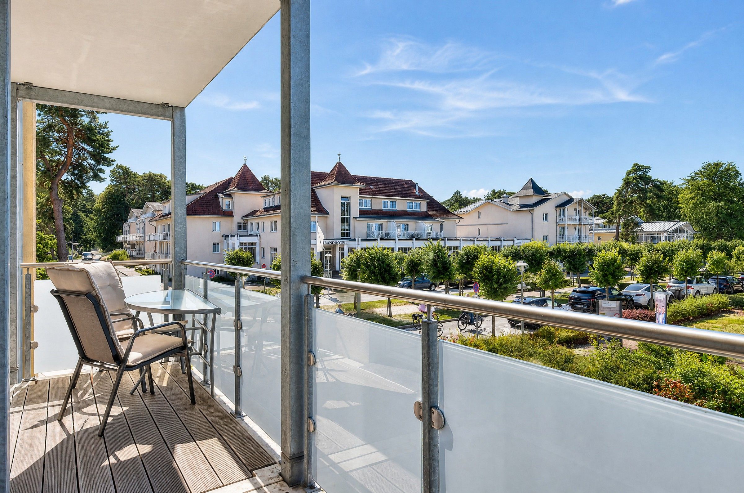 Ein Balkon mit Tisch und Stühlen, der auf einen Parkplatz und Gebäude mit roten Dächern blickt.