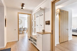 Un corridoio con pavimento in legno, una porta bianca e una zona pranzo con sedie e tavolo.