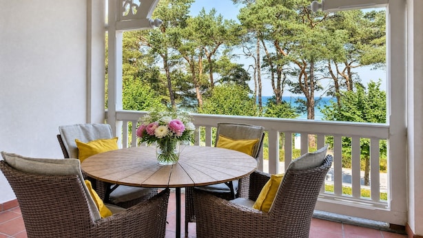 A covered outdoor seating area with a round table and wicker chairs, overlooking a view of trees and a body of water. - Strandlust 610, Villa Seeadler:Unique Baltic Sea view & cozy ambience. (Binz)