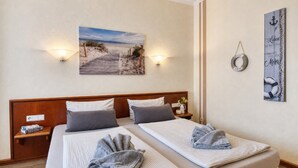 A double bed with two pillows, a bedside table with a book, a wall-mounted picture of a beach, and a life preserver decoration. - Strandlust 610, Villa Seeadler:Unique Baltic Sea view & cozy ambience. (Binz)