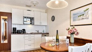 A modern kitchen with white cabinets, a microwave, and a dining area with a wooden table and chairs. - Strandlust 610, Villa Seeadler:Unique Baltic Sea view & cozy ambience. (Binz)