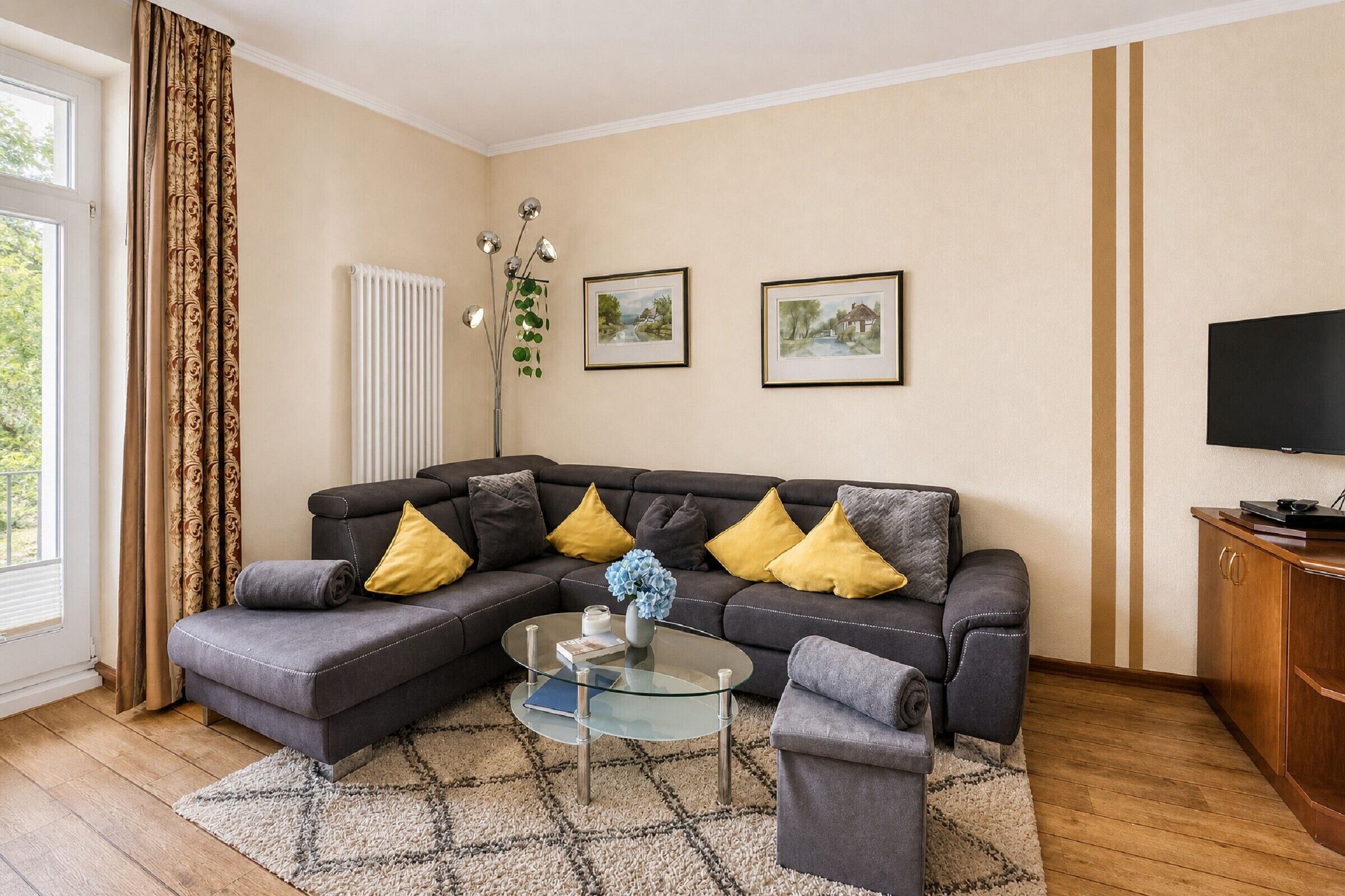 A living room with a sectional sofa, a glass coffee table, a TV, and framed pictures on the wall.
