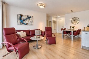 Un salon moderne avec un canapé en cuir rouge, une table basse ronde et un coin repas comprenant une table en bois et des chaises rouges.