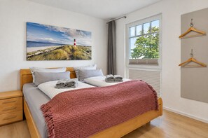 A bedroom with a bed, a window with blinds, a painting, and a wardrobe.
