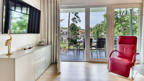 Una sala de estar moderna con un sillón rojo, un mueble blanco y un ventanal con vistas a un balcón con mobiliario exterior.