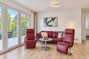 Un salon moderne avec un canapé en cuir rouge, deux fauteuils assortis, une table basse ronde et une œuvre d’art contemporaine accrochée au mur.