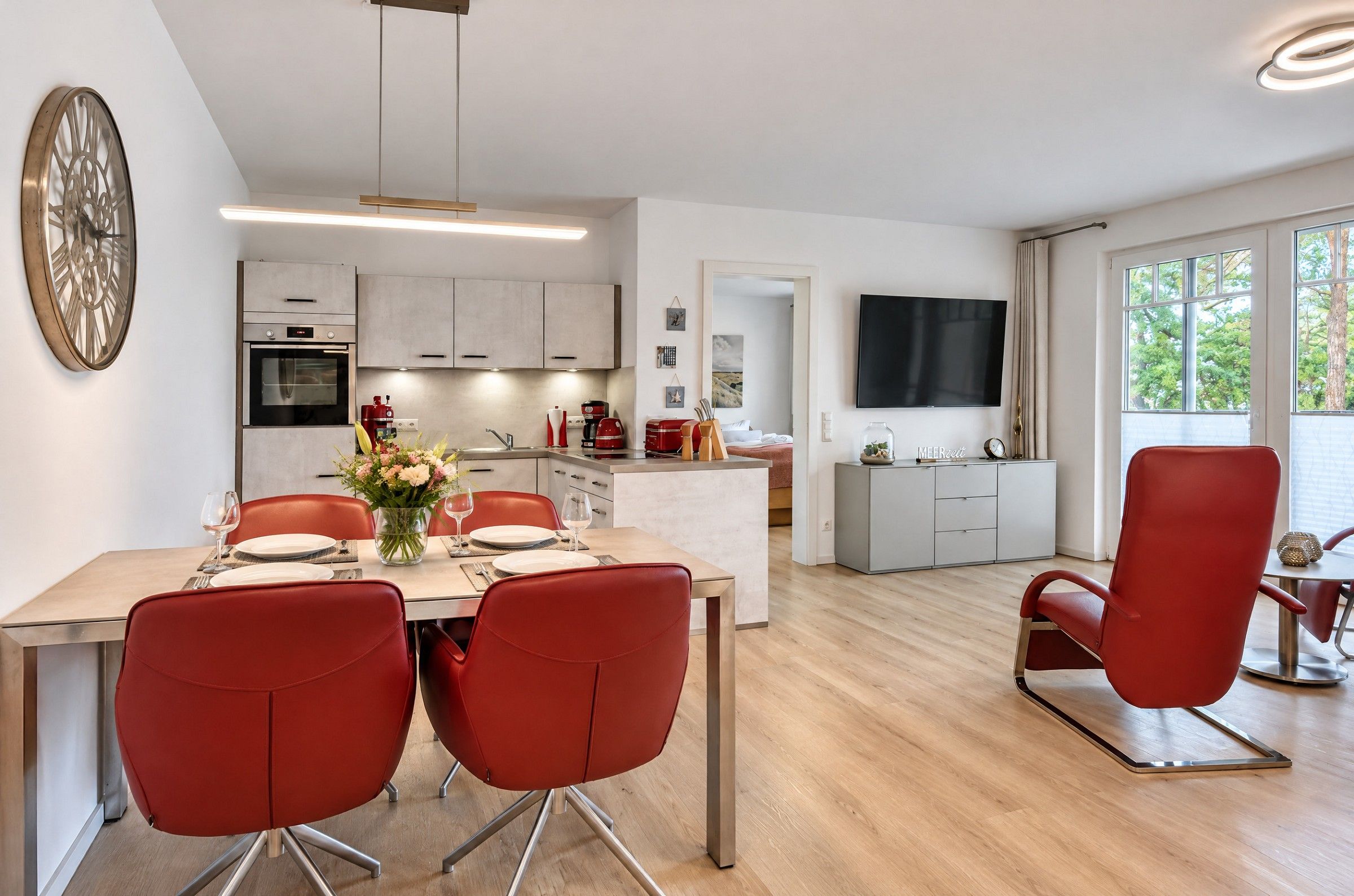Eine moderne Küche mit integrierten Geräten, ein Essbereich mit roten Stühlen und ein Fernseher im Wohnzimmer.