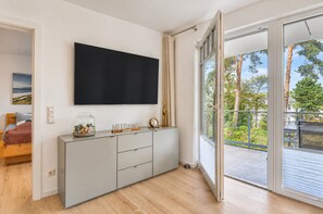 A modern living room with a flat-screen TV mounted on the wall, a grey cabinet with decorative items, and a sliding glass door leading to an outdoor balcony.