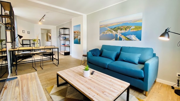 Uma sala de estar moderna com um sofá azul, mesa de centro de madeira e um espaço de jantar com mesa e cadeiras.