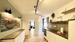 Uma cozinha moderna com piso de madeira, armários brancos, bancada preta e uma grande pintura com vista para a cidade.