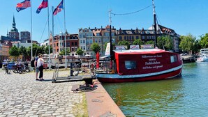 Un bote rojo amarrado en la orilla, con adoquinado y edificios históricos al fondo.