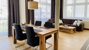 Una sala de estar moderna con una mesa de comedor de madera, sillas negras, un sofá marrón y un ventanal con cortinas translúcidas.