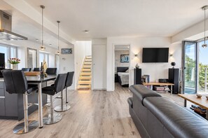A modern living space with a dining area, a sofa, a staircase, and a TV mounted on the wall.