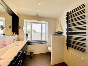 Et moderne badeværelse med et stort spejl, en vask med bordplade, et toilet og et vindue med udsigt.
