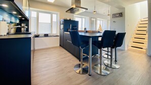 A modern kitchen with a dining area, featuring a central island, bar stools, and a staircase leading to an upper level.