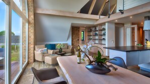 Amplia sala de estar con un ventanal grande, una mesa de comedor con un florero y una zona de cocina con armarios de madera y encimera.