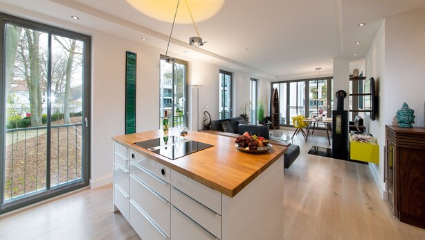 A modern kitchen with a large island, a dining area with a yellow chair, and large windows offering a view of the outdoors. - "My time out": Luxurious wellness suite with pool, sauna & infrared cabin (Binz)
