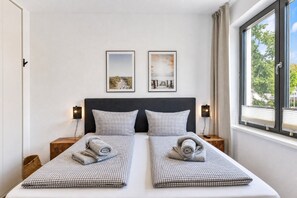 A double bed with checkered bedding, two bedside tables with lamps, and two framed pictures on the wall.