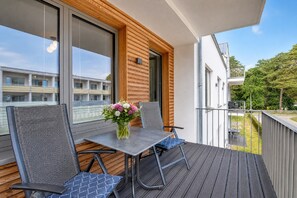 Un balcone con tavolo e due sedie, un vaso con fiori e vista su un edificio residenziale.