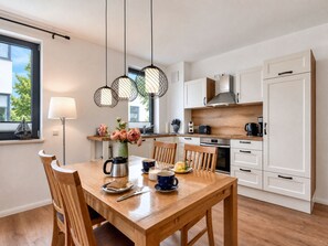 A modern kitchen with white cabinets, a wooden dining table, and pendant lights.