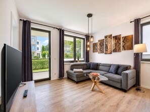 A modern living room with a sofa, a glass coffee table, a TV, and artwork on the wall.