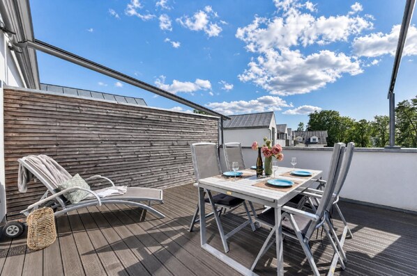 Una terraza en la azotea con una mesa lista para comer, una silla de lounge y vistas al cielo.