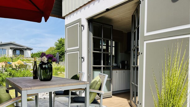 Une terrasse ouverte avec une table et des chaises, une plante en pot et une vue sur la cuisine.