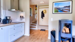 Une cuisine moderne avec des meubles blancs, une machine à café et une cuisinière. Un escalier mène à une chambre à coucher où se trouvent un lit et un tableau représentant un pont.