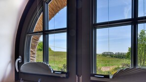 A room with large windows, a wooden floor, and a thatched roof visible through the window. - Newly built, modern, exclusive - that describes the Klein Stresow vacation village (Klein Stresow)