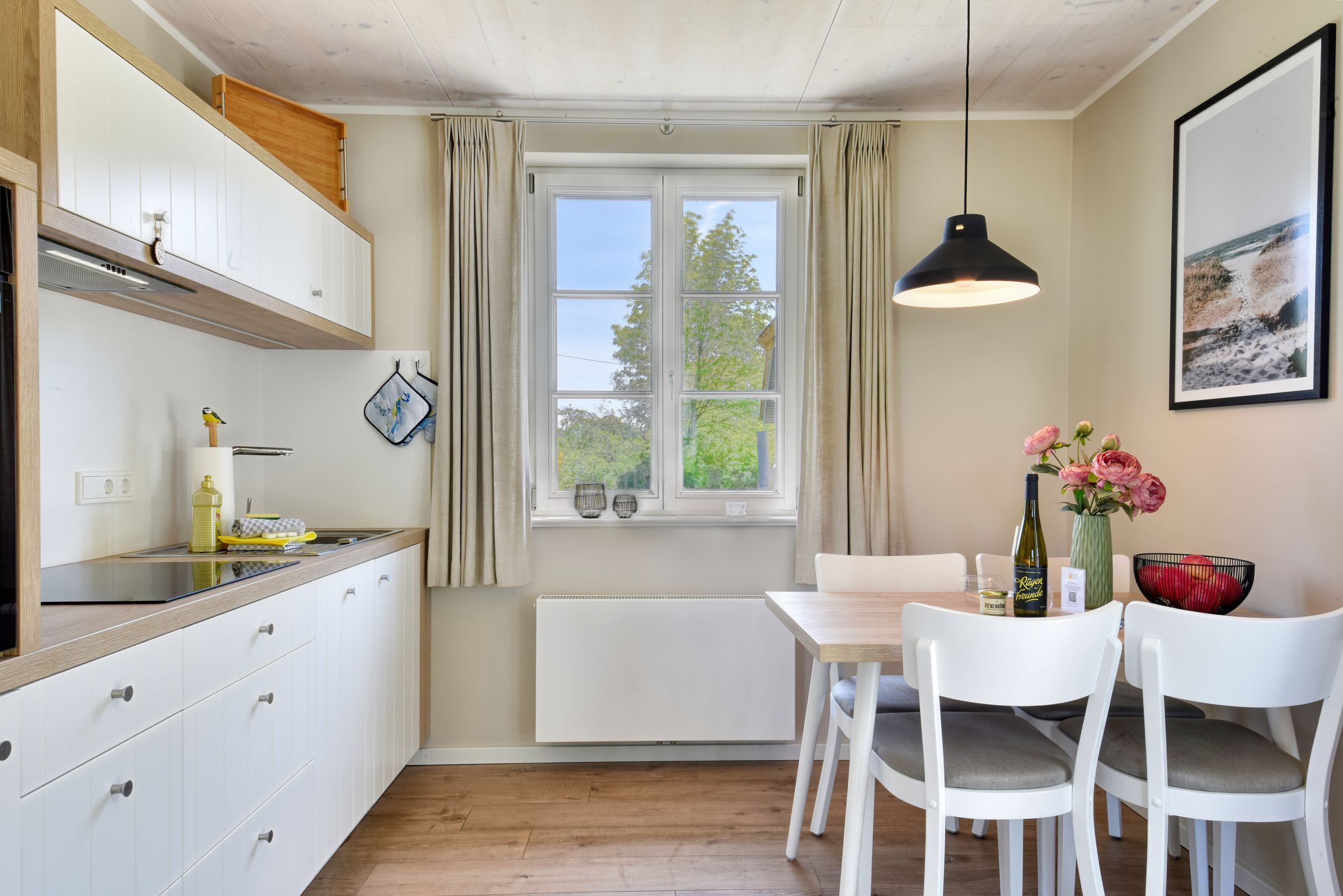 A kitchen with a window, white cabinets, a dining table with chairs, and a hanging pendant light.