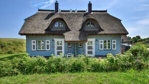 A two-story house with a steeply pitched roof, multiple chimneys, and a front porch with two chairs. - Newly built, modern, exclusive - that describes the Klein Stresow vacation village (Klein Stresow)