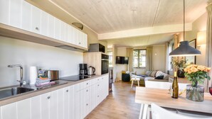 Cozinha moderna com armários brancos, bancada de madeira e área de jantar com mesa e cadeiras.