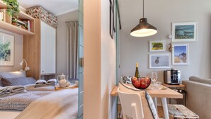 Una habitación de hotel moderna con cama, mesita de noche y zona de comedor con mesa, sillas y cafetera.