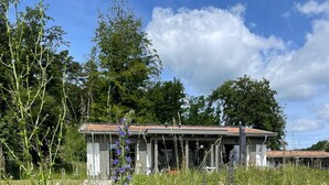 Un edificio rústico con techo inclinado, rodeado por un campo exuberante de flores silvestres y hierbas altas.