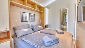 A bedroom with two beds, wooden shelving, framed pictures, and a mirror.
