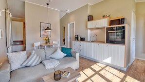A modern living room with a sofa, coffee table, and a kitchen area with cabinets and appliances.