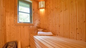 A wooden cabin room with a bed, a window, and a wall-mounted light fixture.