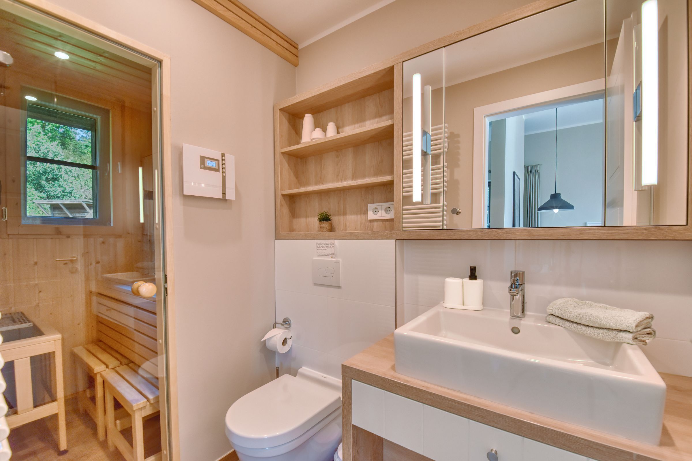 A modern bathroom with a wooden bench, a bidet, a sink, and a large mirror.