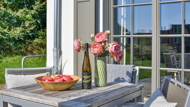 A wooden table with a bowl of apples, a bottle of wine, and a vase with flowers.