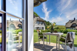 A patio with a table and chairs, a vase with flowers, and a view of a house with a thatched roof. - Newly built, modern, exclusive - that describes the Klein Stresow vacation village (Klein Stresow)