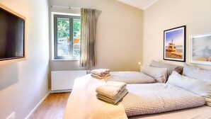 Quarto com duas camas, janela com cortinas, televisão de tela plana e quadros na parede.