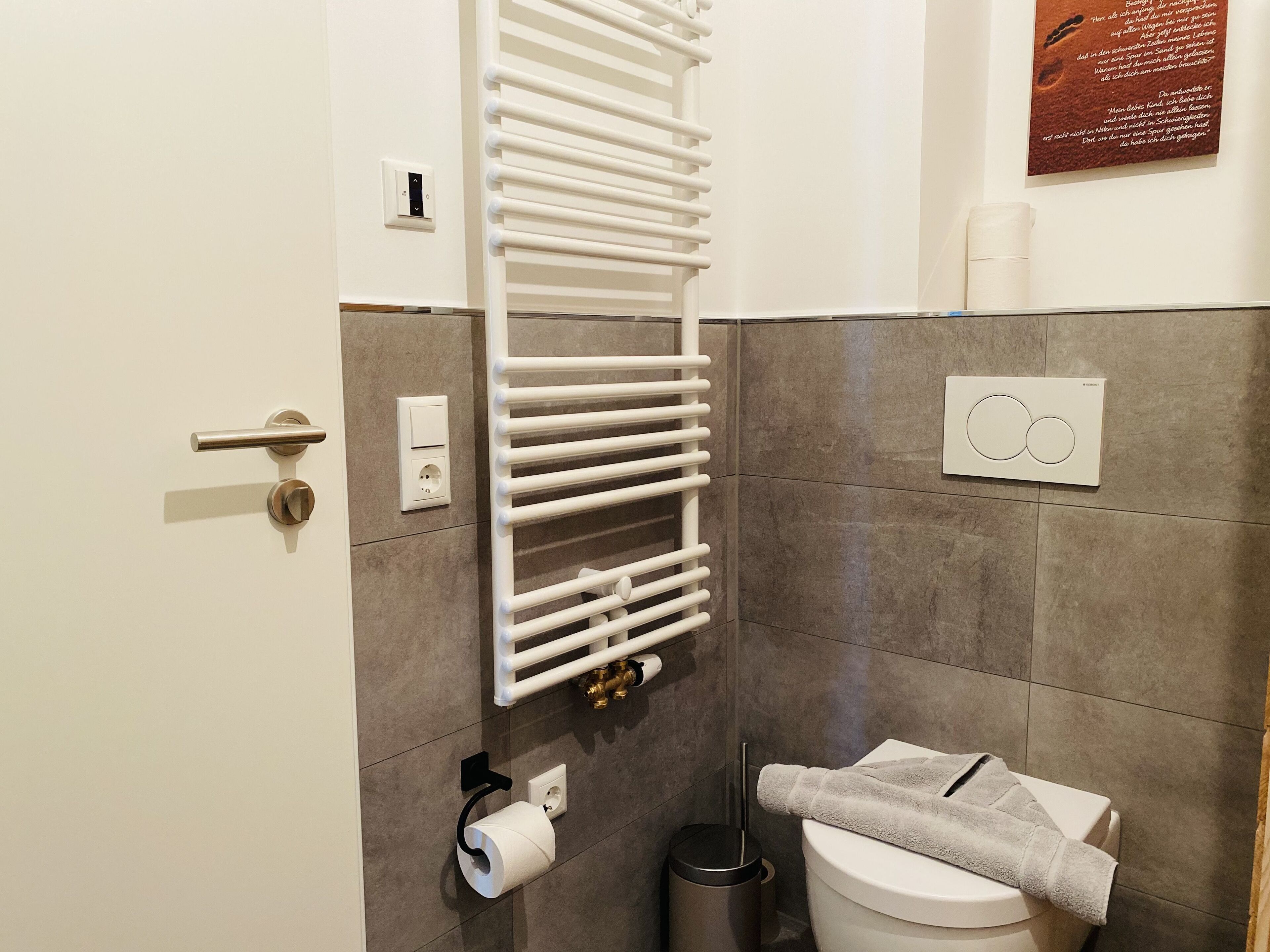 Un baño con toallero, papel higiénico y calefactor en la pared.